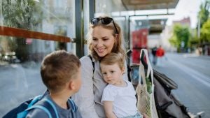 a mother and her kids waiting at a bus stop with a stroller on the side