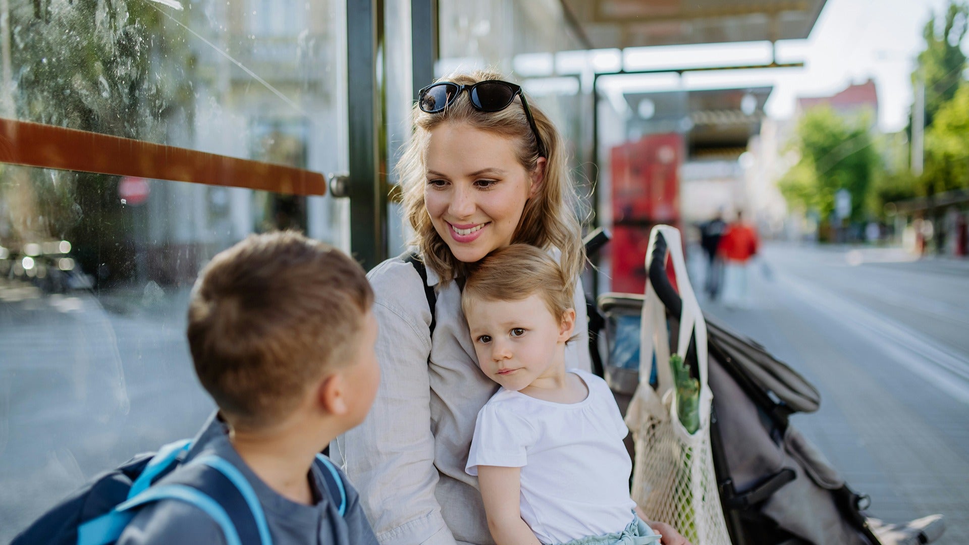 a mother and her kids waiting at a bus stop with a stroller on the side