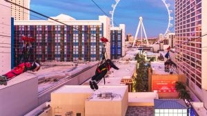 people ziplining to a large ferris wheel over the city