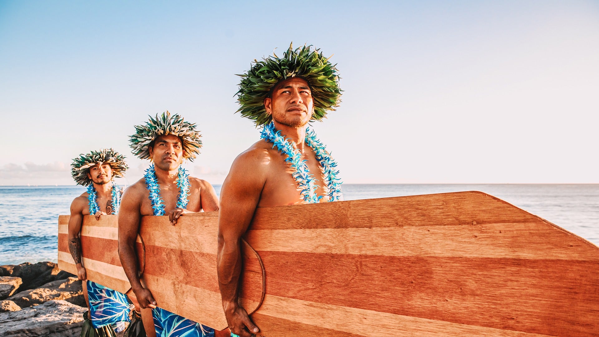 group of men wearing headdresses and leis holding a wooden board