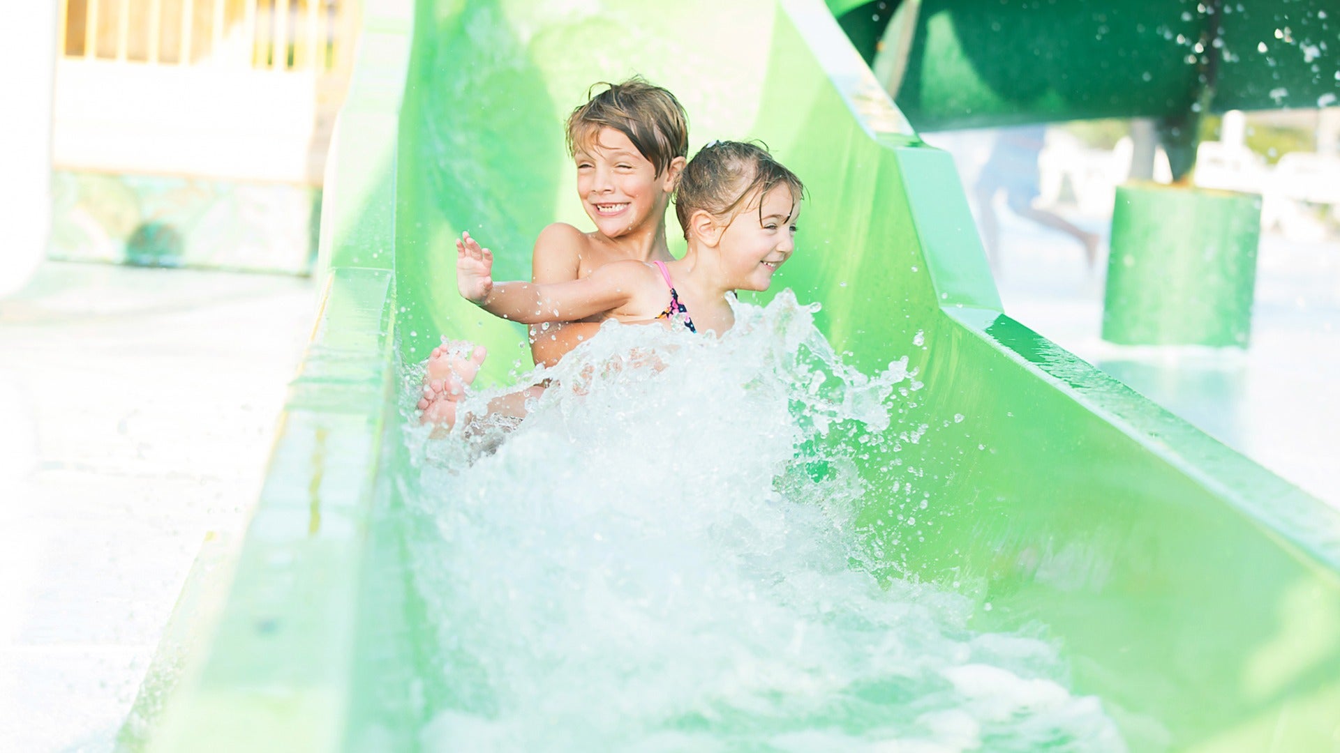 siblings enjoying going down a slide in a water park