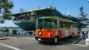 a tour trolley with passengers and the USS midway museum at the back