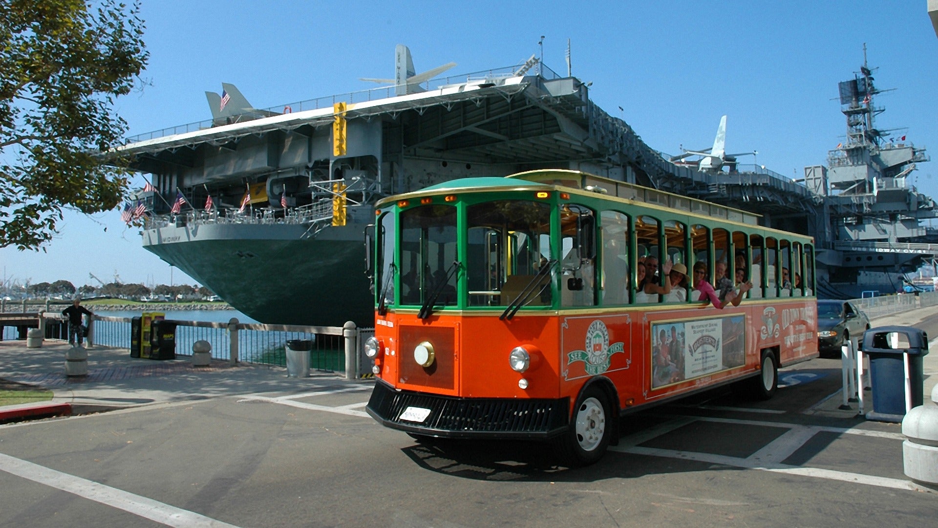 a tour trolley with passengers and the USS midway museum at the back