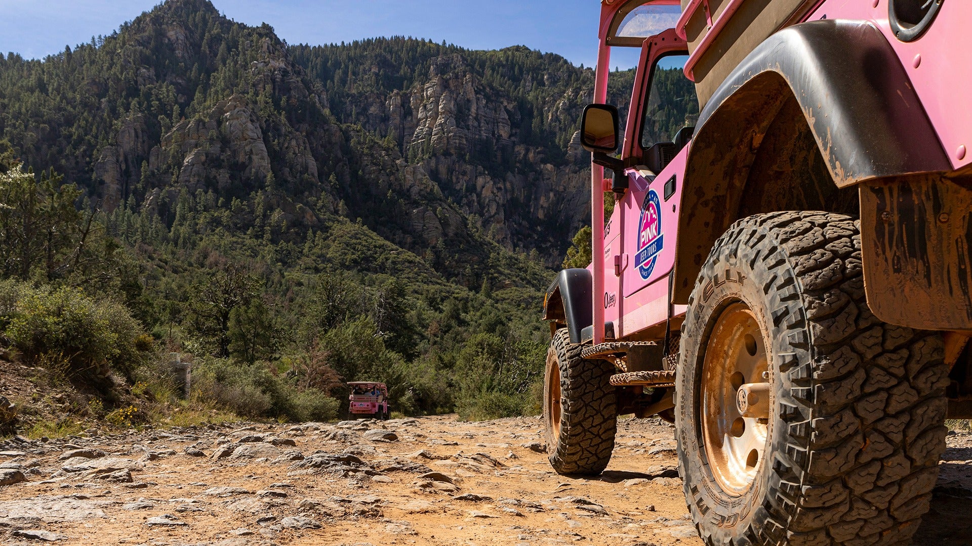 a pink jeep driving off road into a mountainous area