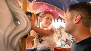 father and daughter on a carousel ride, the girl is wearing mickey ears