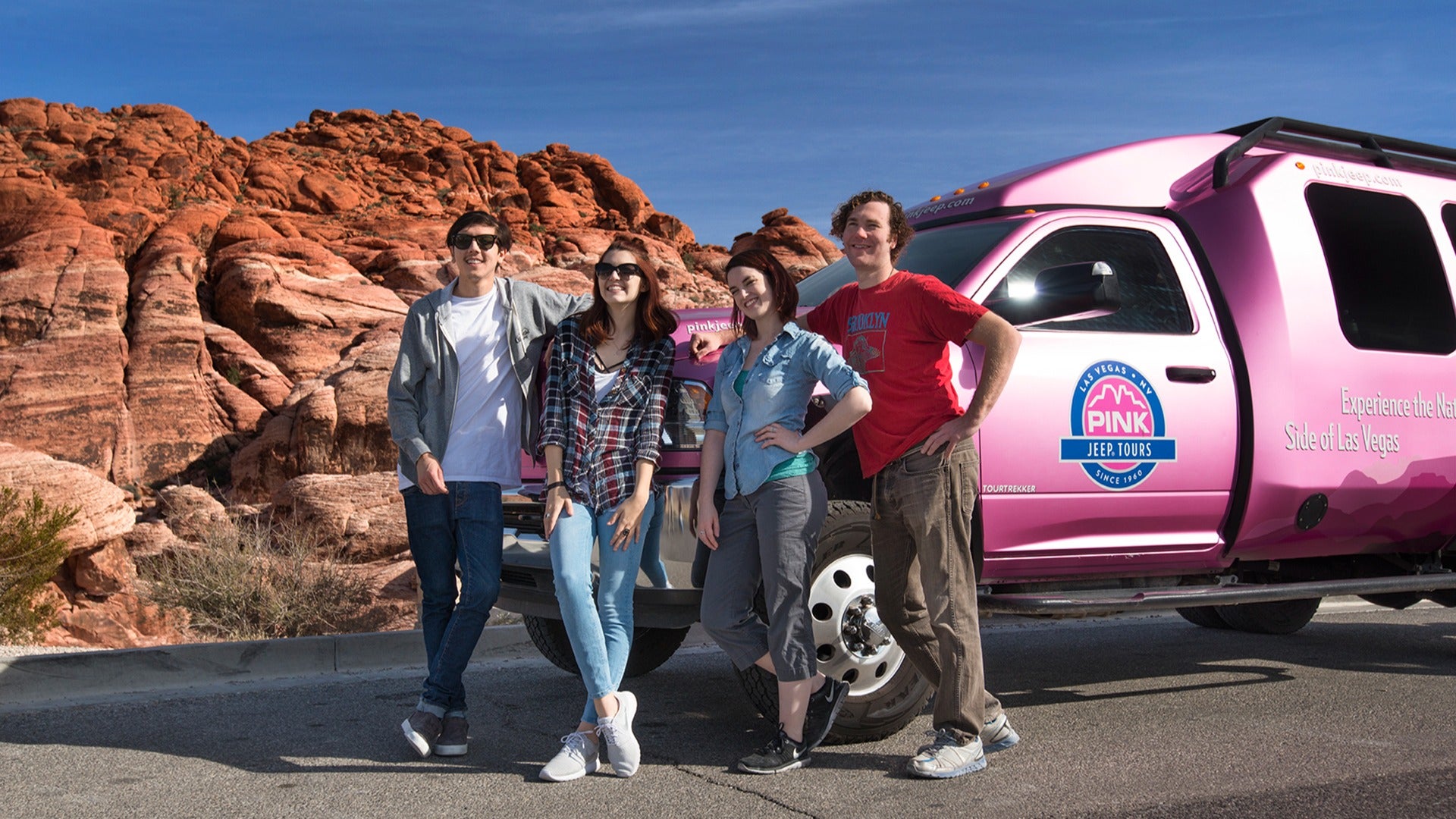 a group of people in front of a pink jeep with red rocks behind them