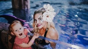 a mermaid in a water tank exhibit posing with a child