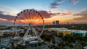 a ferris wheel aerial view with the ocean and sunset behind