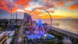 a ferris wheel at sunset with a view of the ocean and city beyond it