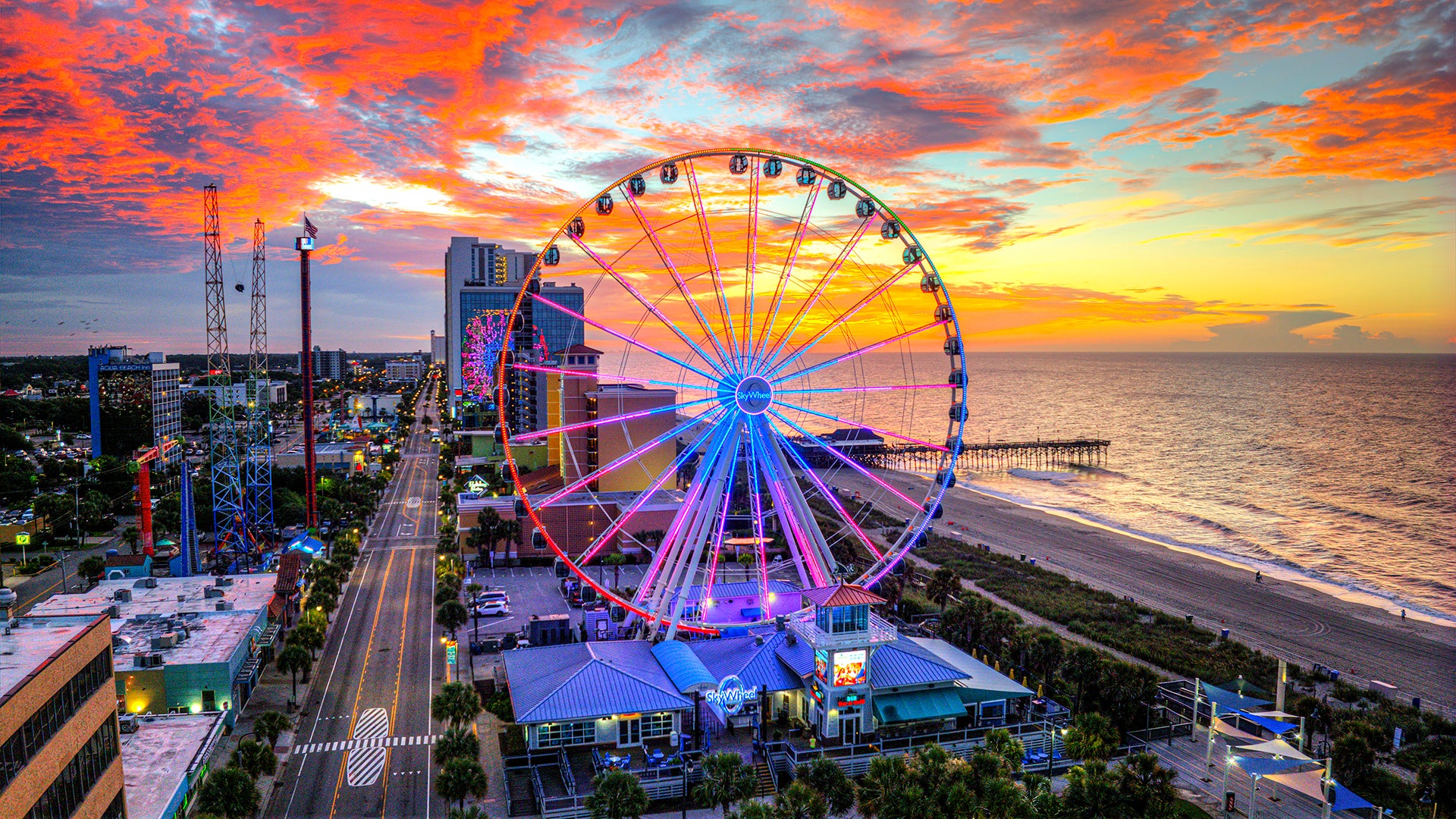 a ferris wheel at sunset with a view of the ocean and city beyond it