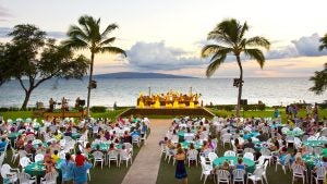 a luau with performers and a big audience and a view of the ocean behind