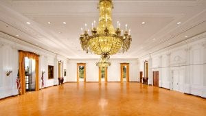 a spacious hall with a large chandelier, white walls, USA flags and windows