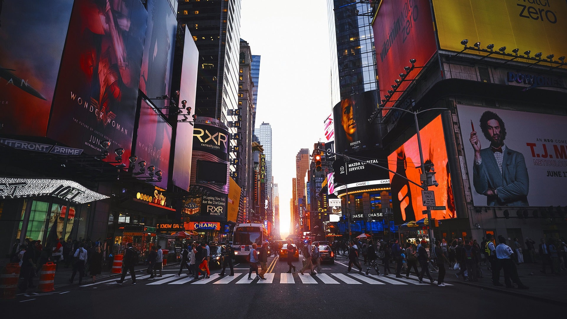 a crosswalk with people crossing and various billboards across the city
