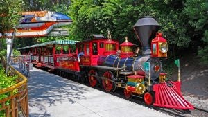 red steam train with passengers passing by trees