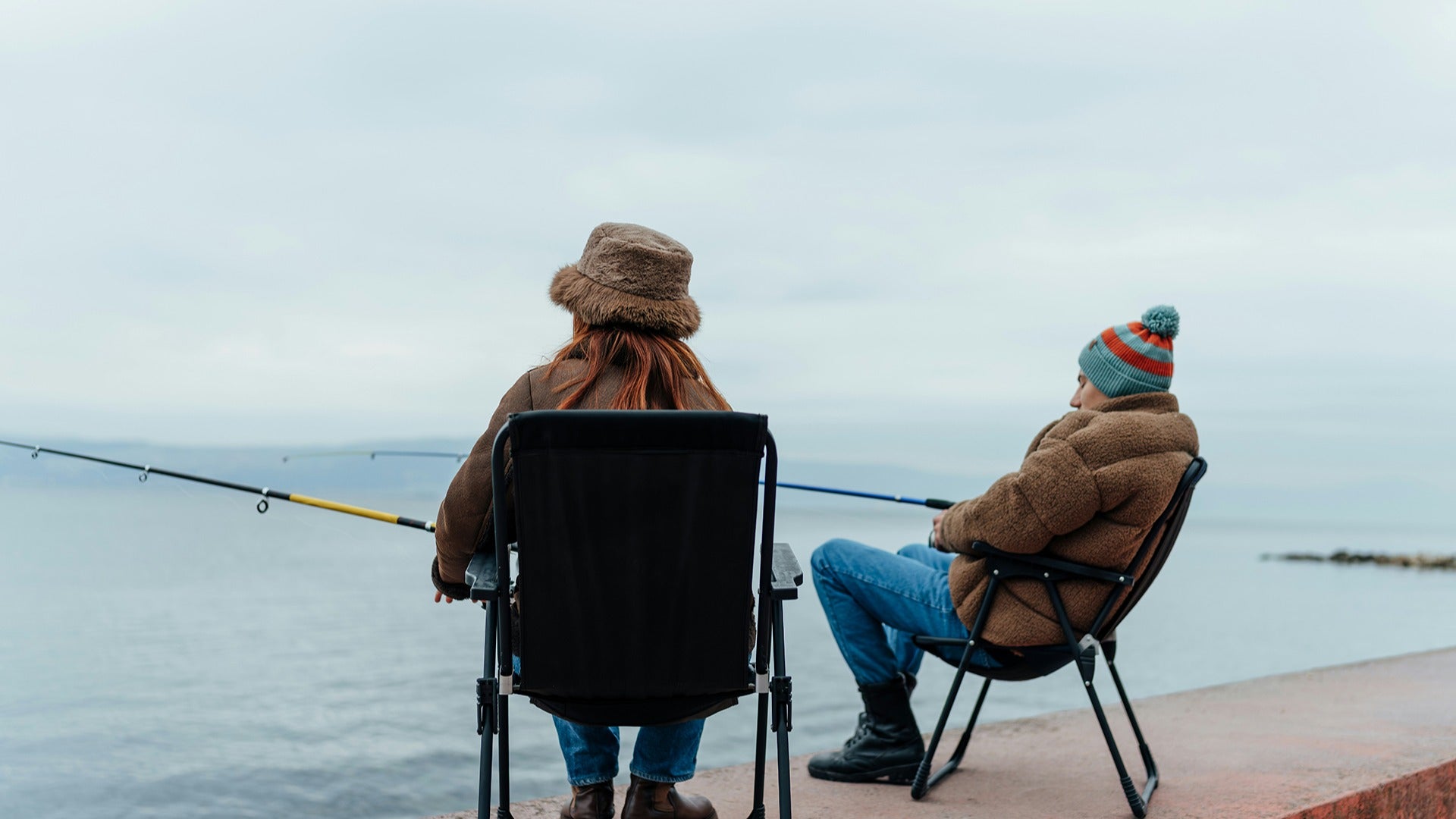 a couple wearing winter clothes fishing on the ocean
