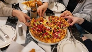 group of friends eating pizza with other food on the table, plates, and dinnerware