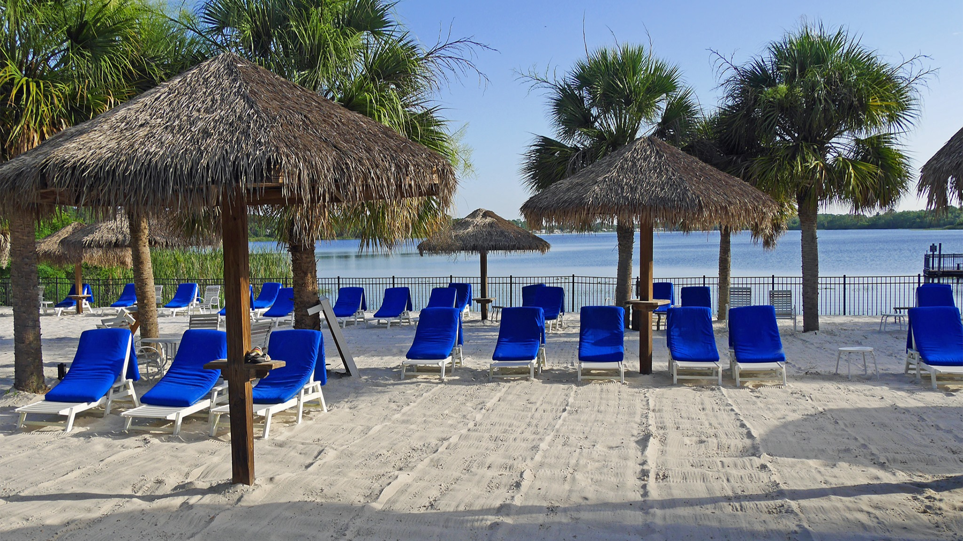 pool chairs and cabanas on a sandy surface with a view of lake behind