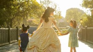 disney princess belle wearing a gown, holding hands with two kids