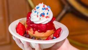 a fourth of july dessert with a muffin, topped with strawberries, whipped cream, and star sprinkles