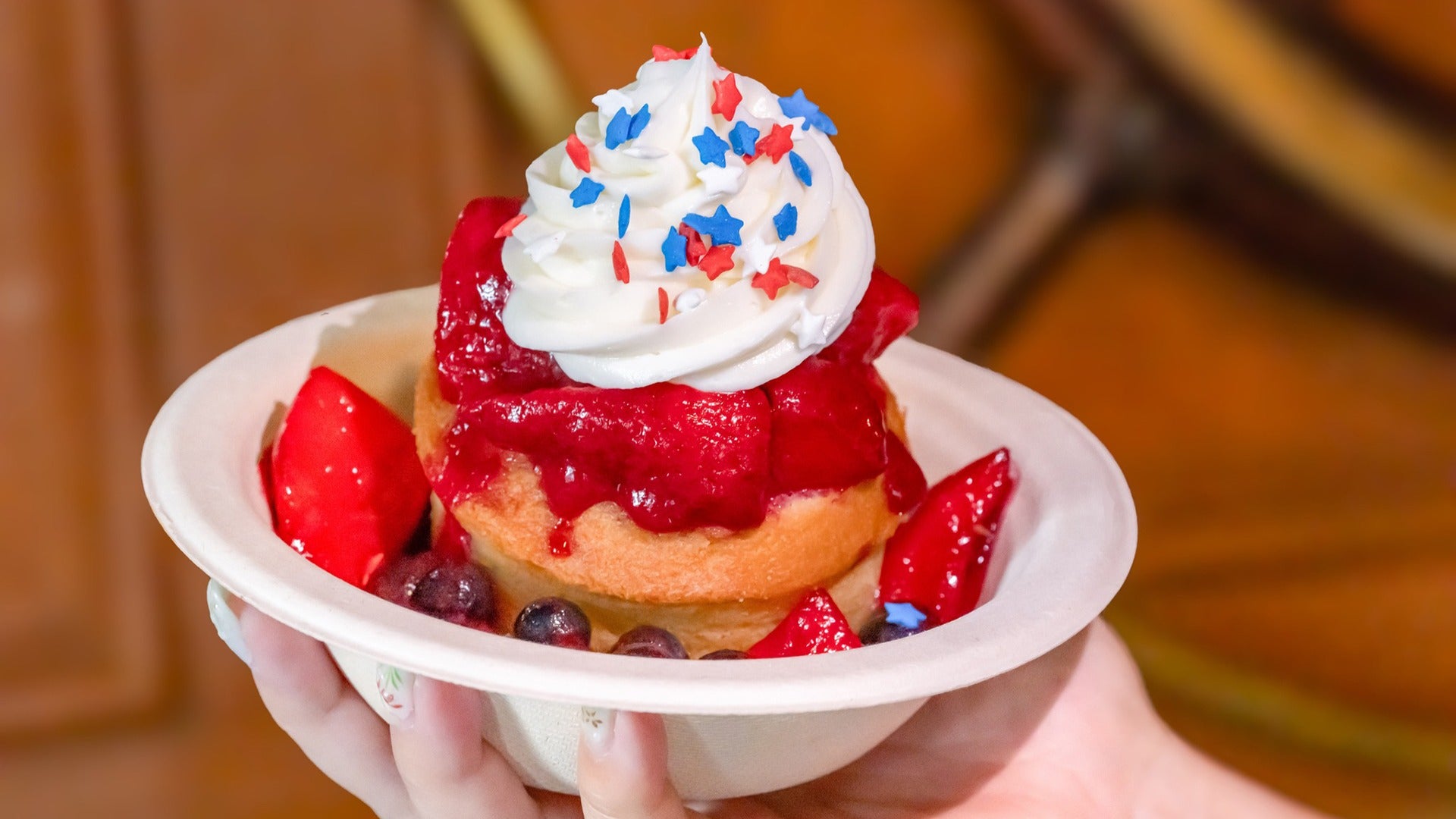 a fourth of july dessert with a muffin, topped with strawberries, whipped cream, and star sprinkles