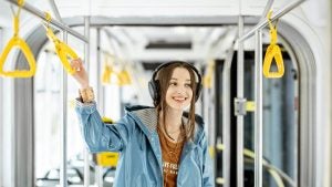a girl wearing headphones holding on a trolley handrail on a commute
