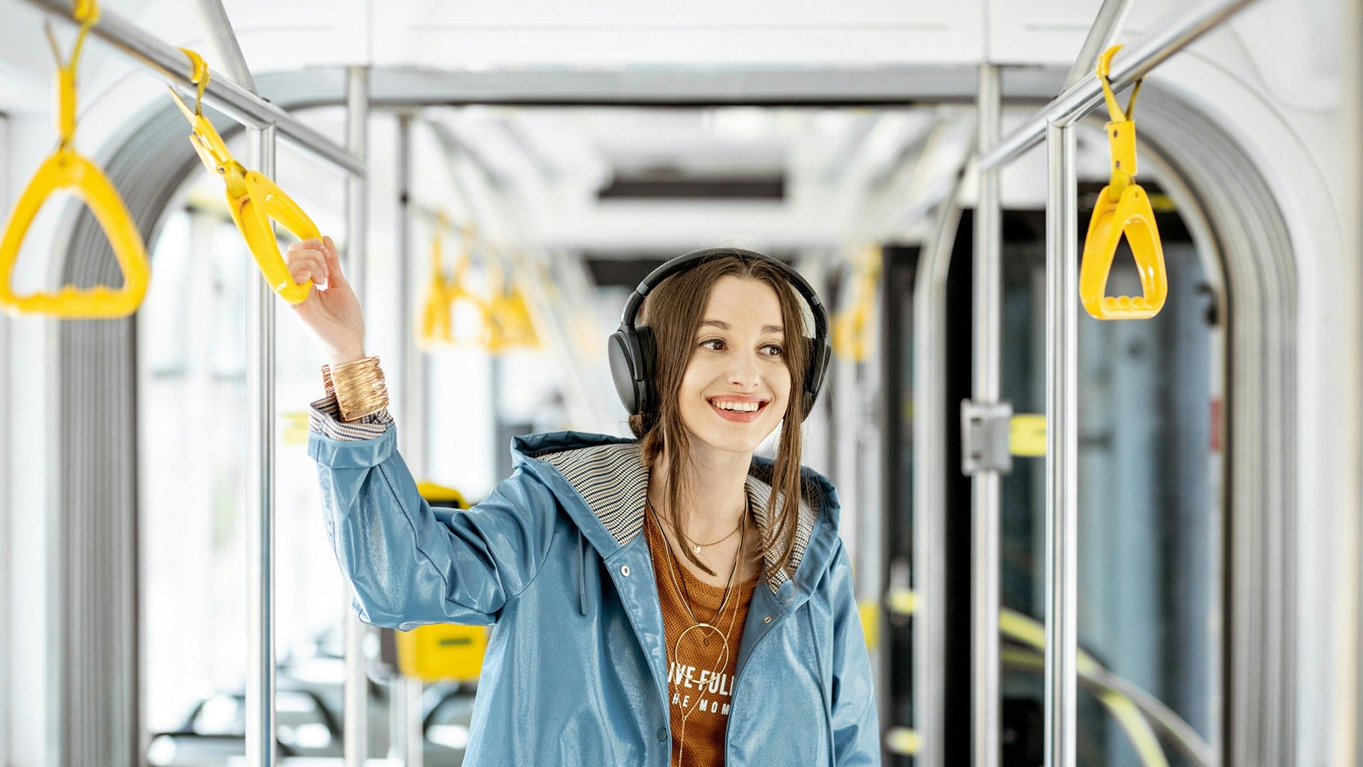 a girl wearing headphones holding on a trolley handrail on a commute