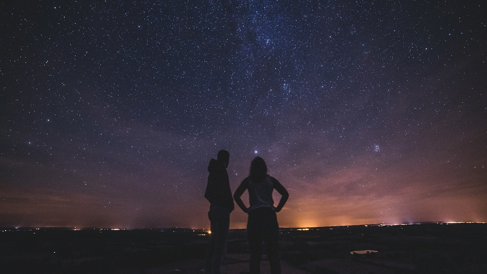 a couple stargazing with city lights below