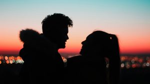a couple staring at each other with the city lights and sunset at the back