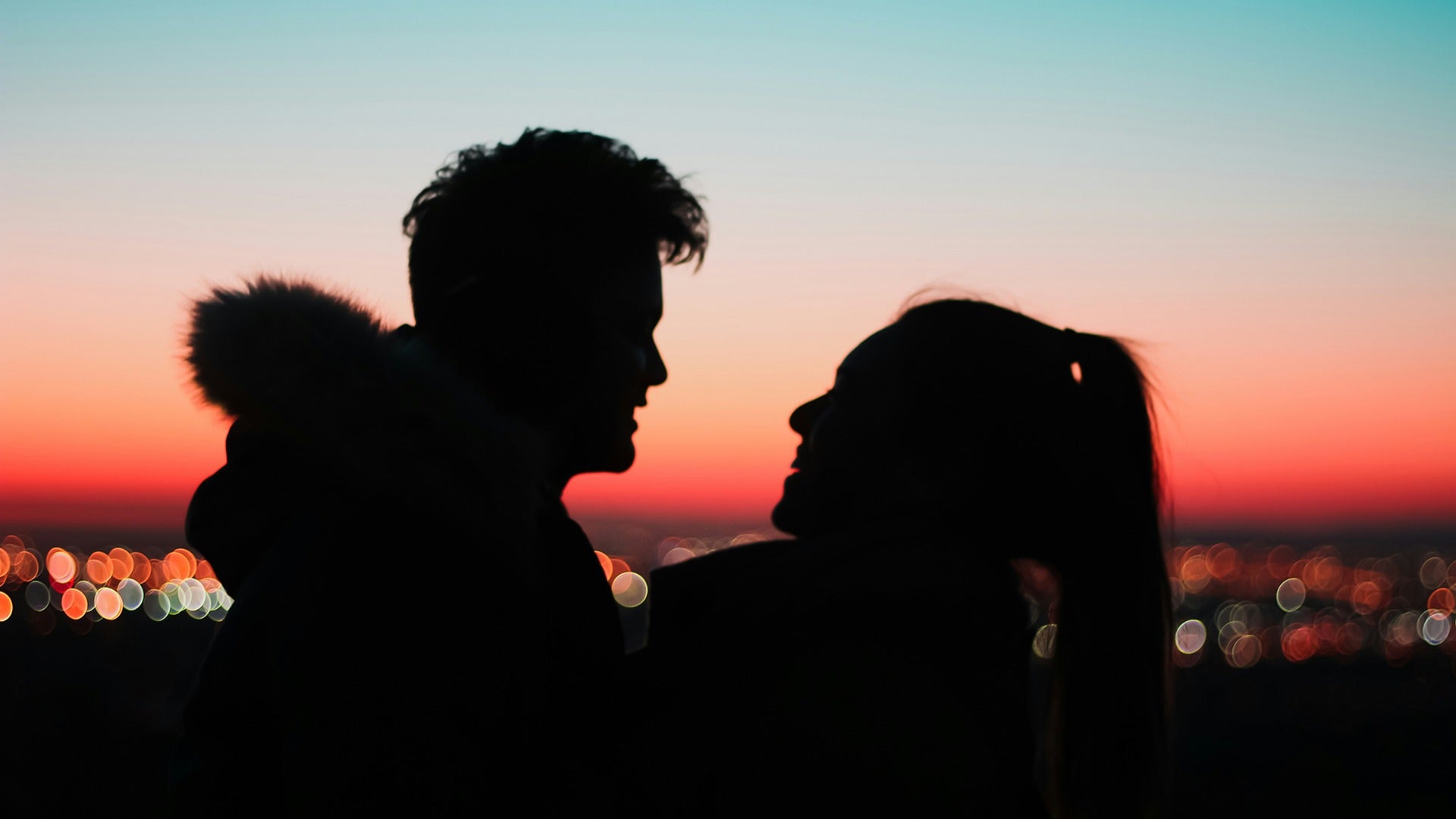a couple staring at each other with the city lights and sunset at the back
