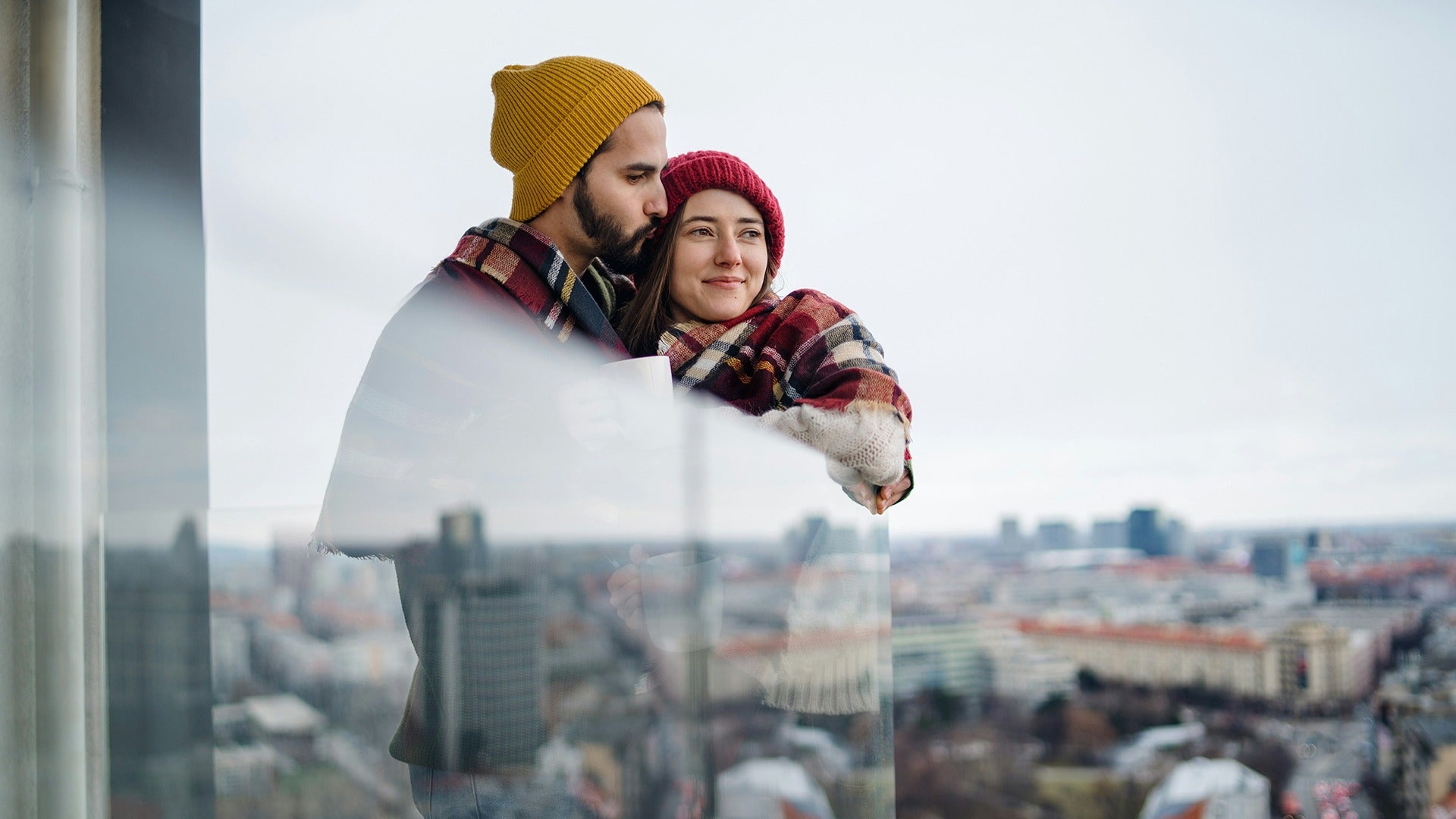 a couple sharing a blanket and wearing beanies overlooking the city
