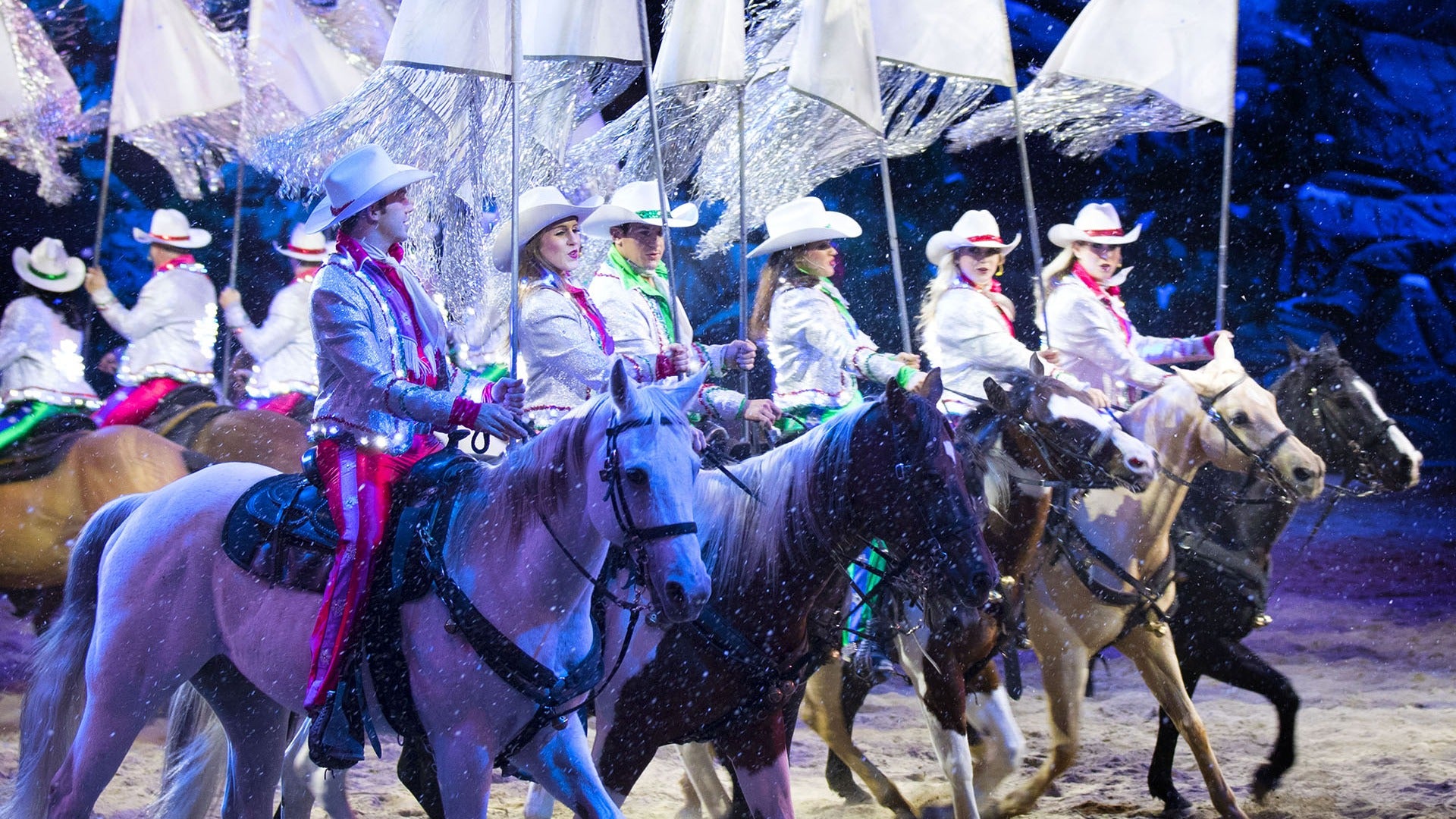 a group of performers wearing costumes riding on horses and carrying white flags
