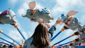 a little girl wearing mickey ears looking up at the dumbo ride in magic kingdom