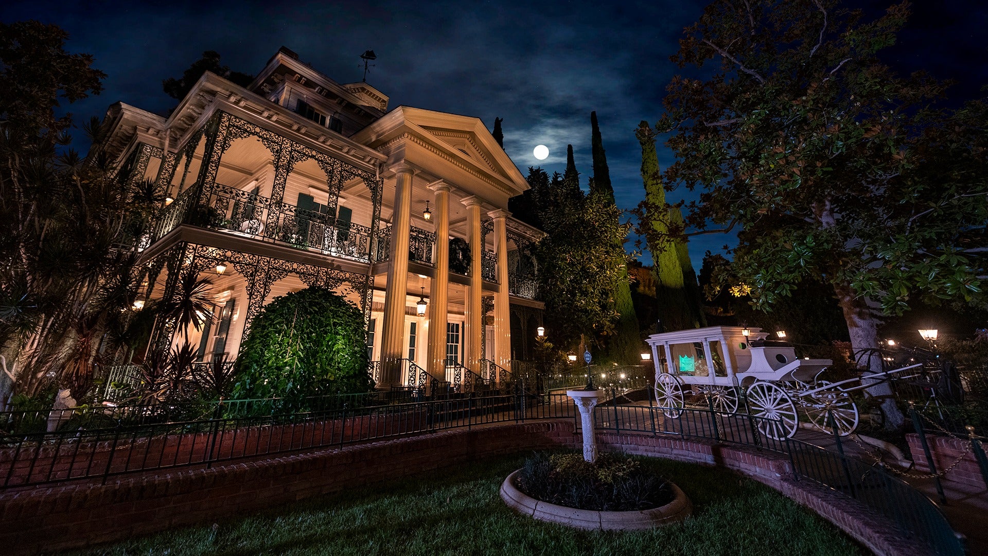 a haunted mansion with a view of the full moon and a white carriage parked in the front lawn
