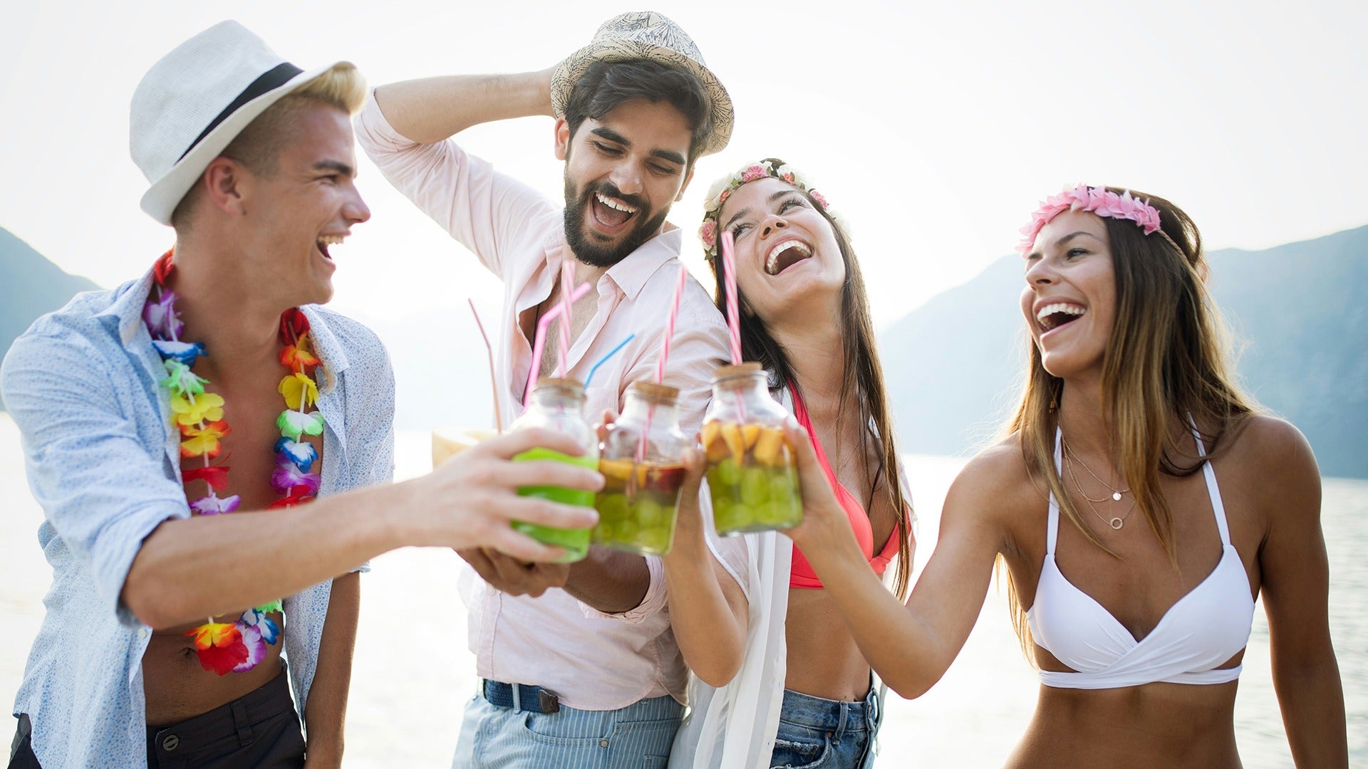 people partying and drinking cocktails while wearing leis and the ocean at the back