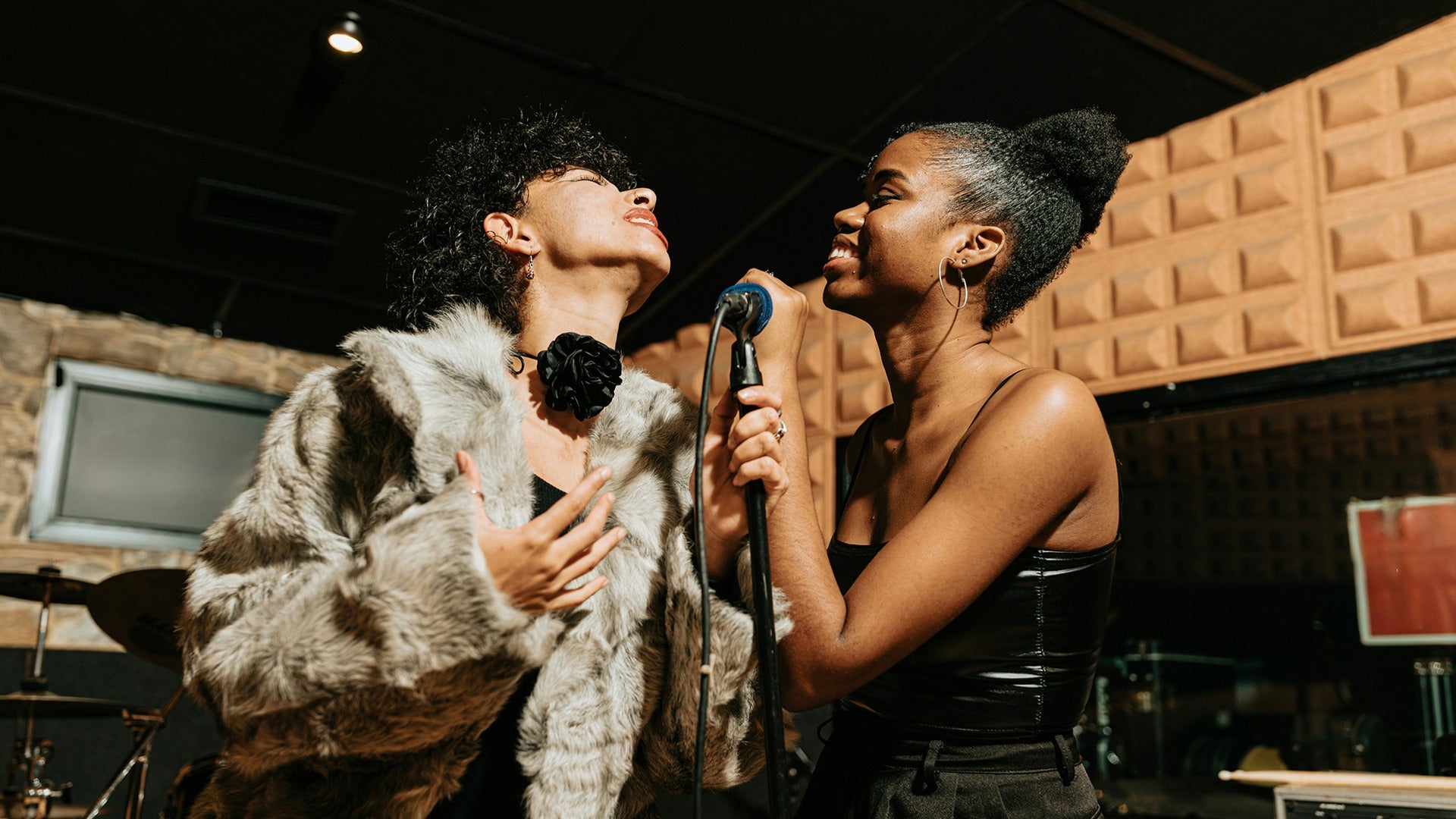 two girls singing in a karaoke room holding microphones
