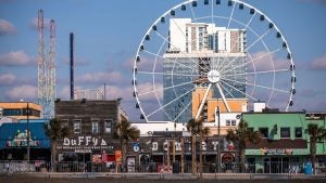a ferris wheel at the back of a beach boardwalk lined with shops