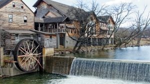 an old large water wheel with trees on the side and people at the viewing deck