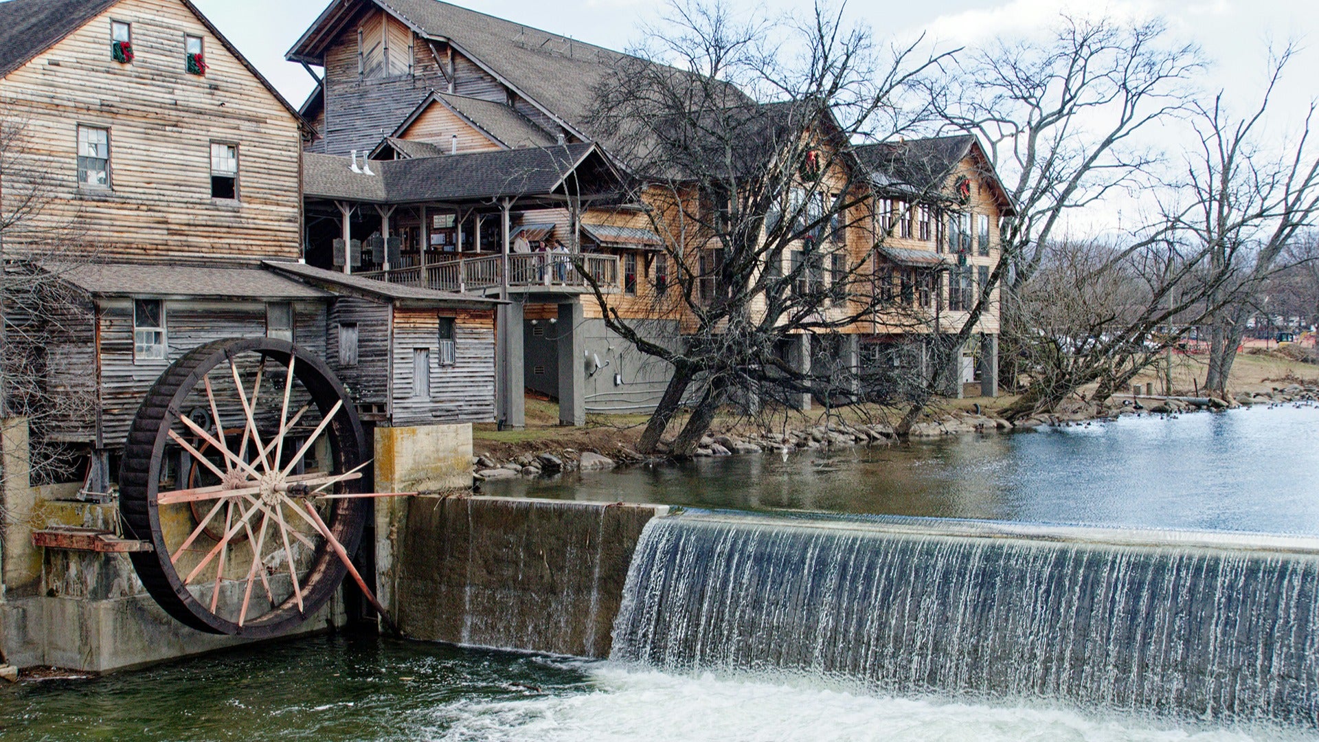 an old large water wheel with trees on the side and people at the viewing deck