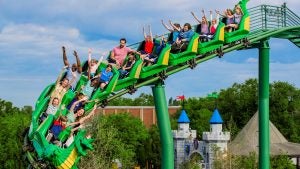 people raising hands in a roller coaster with a view of a castle below