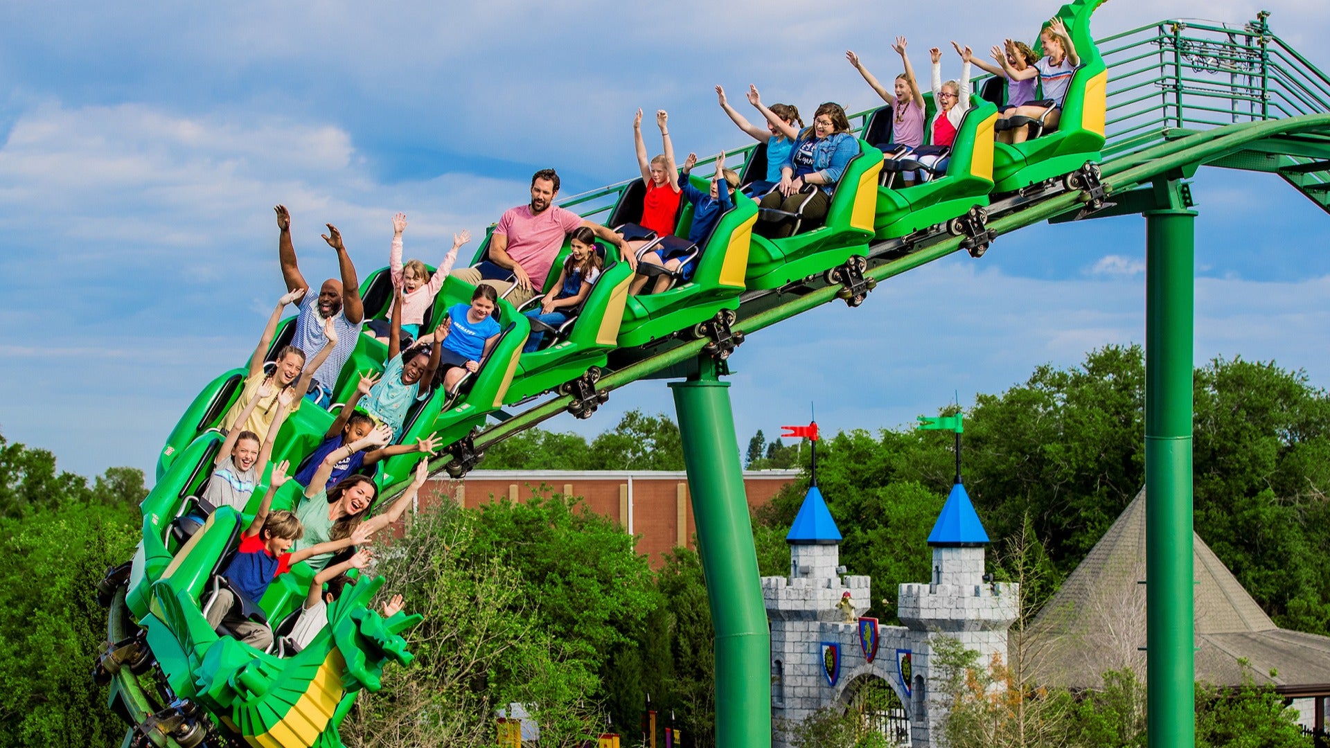 people raising hands in a roller coaster with a view of a castle below