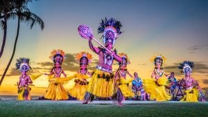 luau performers on stage, with dancers in costumes and singers at back while sunset