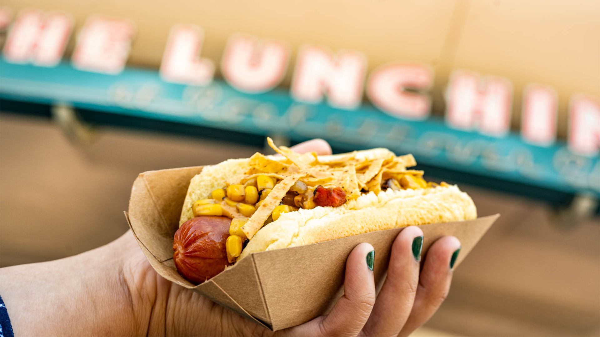 a hand holding a hotdog with toppings with the lunching pad at the back
