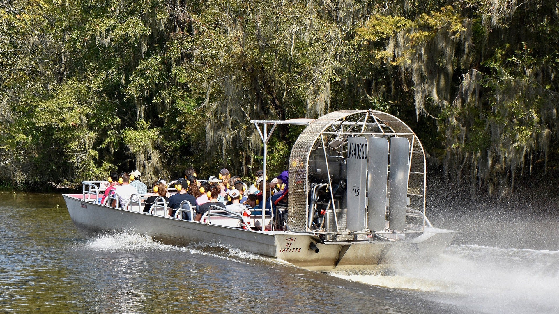 people aboard an airboat riding through a swamp with trees surrounding it