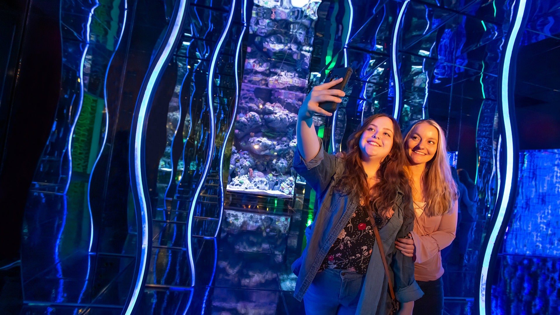 two women snapping pics in front of an aquarium feature