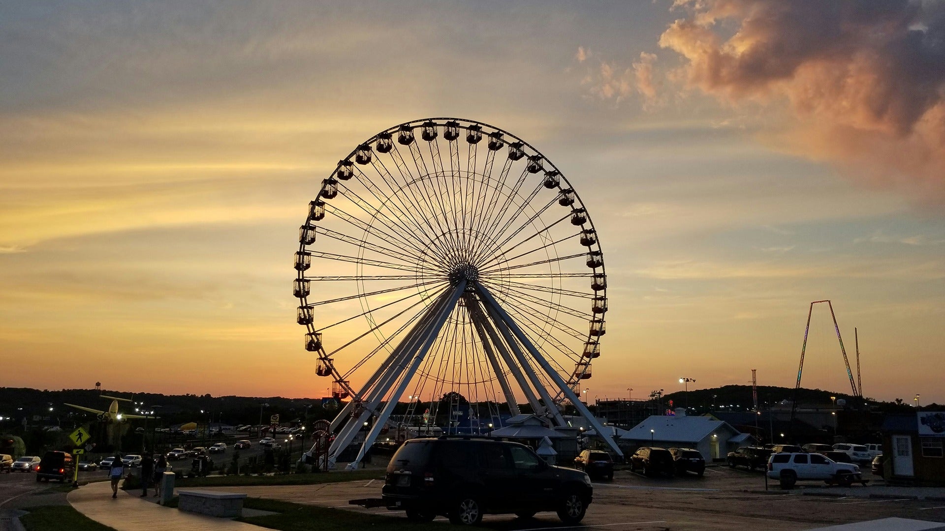 a ferris wheel set against the sunset with a view of the parking lot below