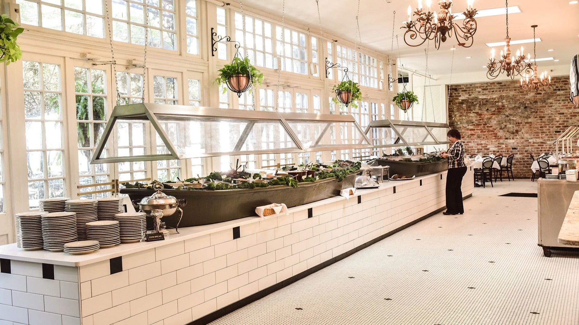 a brunch buffet with a customer getting some food, white tiles and chandeliers on the side