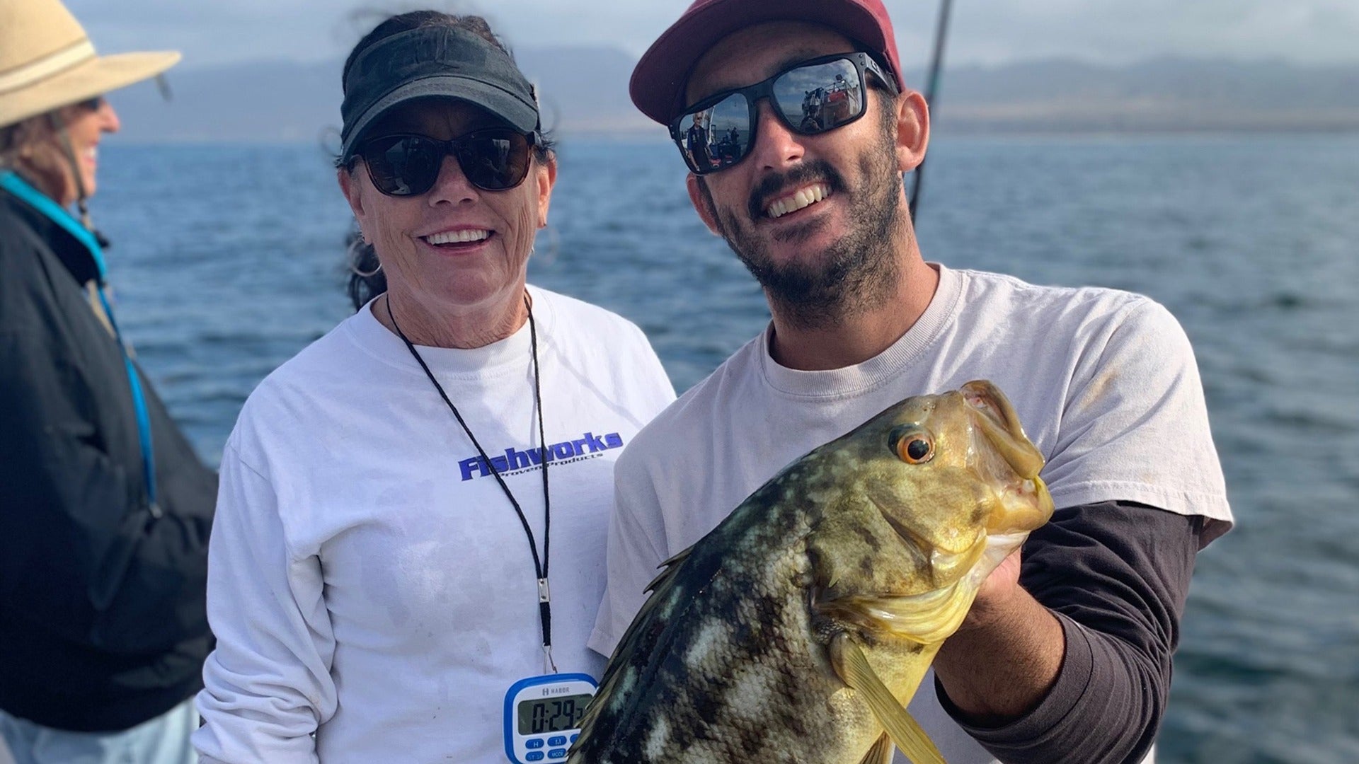 two people smiling at the camera, the other one holding a fish he caught