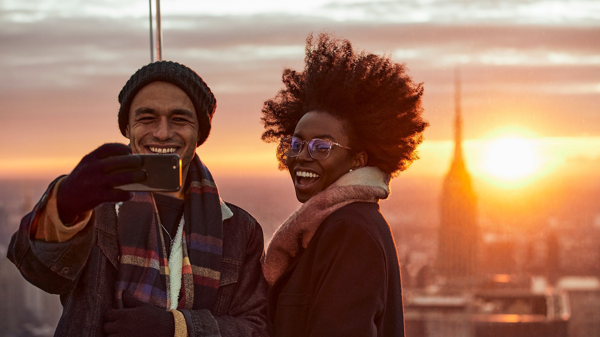 a couple taking a photo on top of a building with a view of the sunset