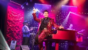 a singer in costume sitting on a piano and performing on stage