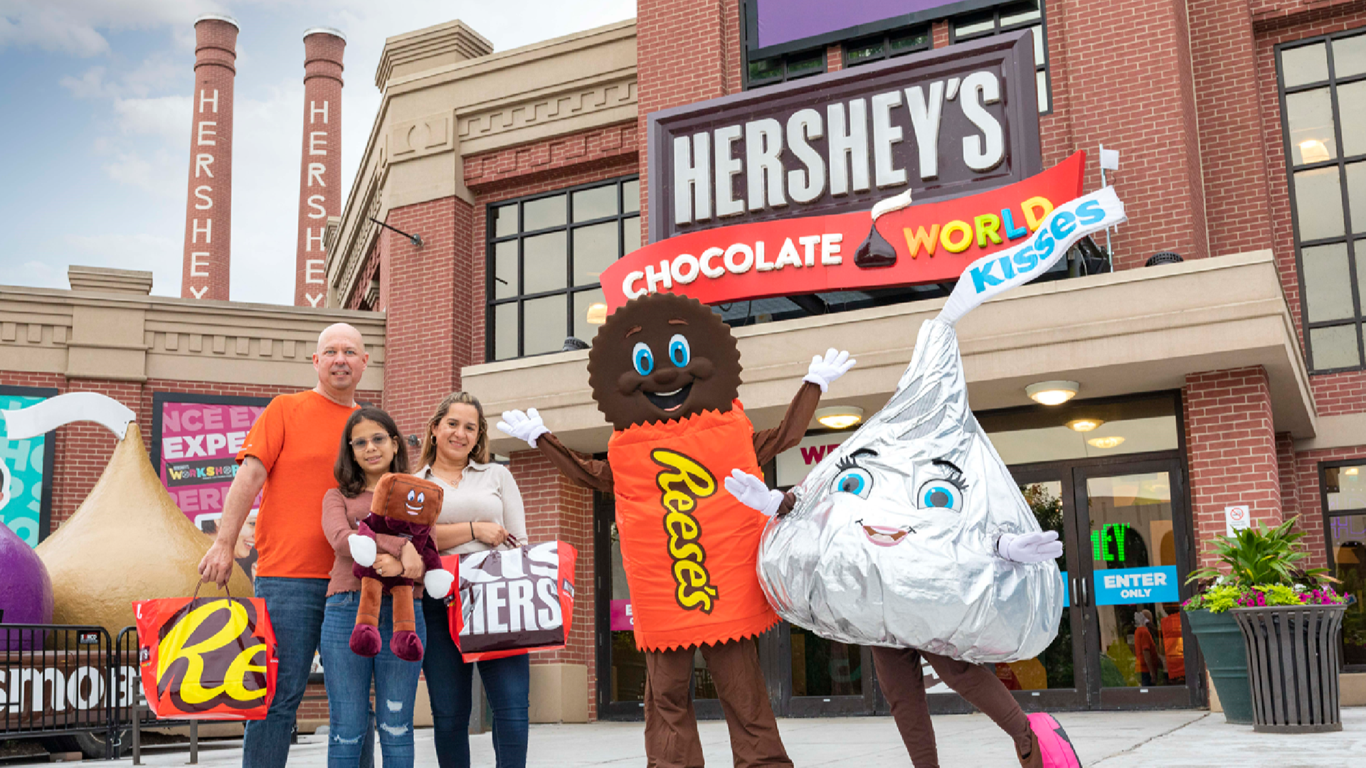 a family with mascots for reese's and hershey's kisses standing in front of hershey's chocolate world